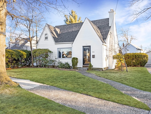 view of front of house with a shingled roof, a chimney, and a front lawn