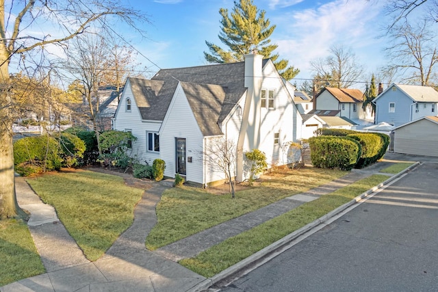 view of side of property featuring a chimney, a residential view, a lawn, and roof with shingles