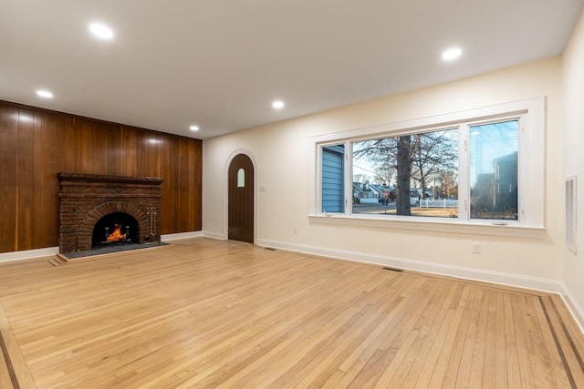 unfurnished living room featuring arched walkways, light wood-style flooring, recessed lighting, visible vents, and a brick fireplace