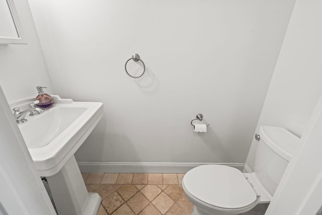 bathroom with stone finish floor, a sink, toilet, and baseboards