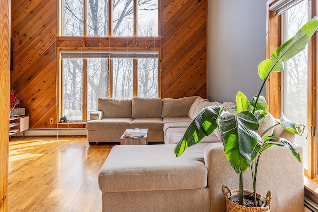 living room featuring a baseboard heating unit, wooden walls, wood finished floors, and a high ceiling