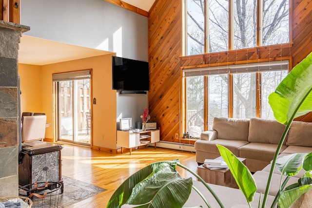 living room featuring a high ceiling, wooden walls, wood finished floors, and baseboard heating