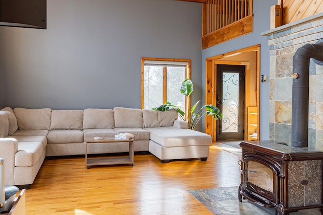 living room featuring a wood stove, a towering ceiling, and light wood finished floors