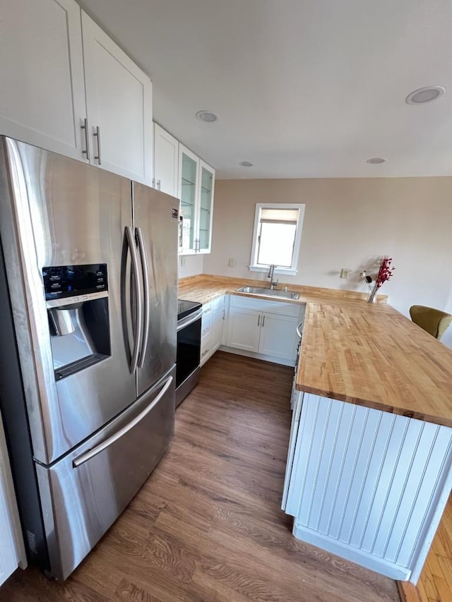 kitchen featuring glass insert cabinets, appliances with stainless steel finishes, a peninsula, wood counters, and a sink