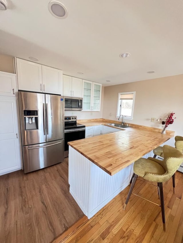 kitchen featuring wooden counters, a peninsula, a sink, glass insert cabinets, and appliances with stainless steel finishes