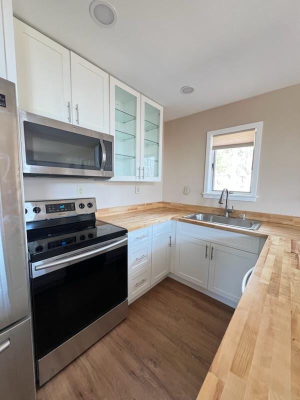 kitchen with a sink, wood counters, dark wood finished floors, stainless steel appliances, and glass insert cabinets