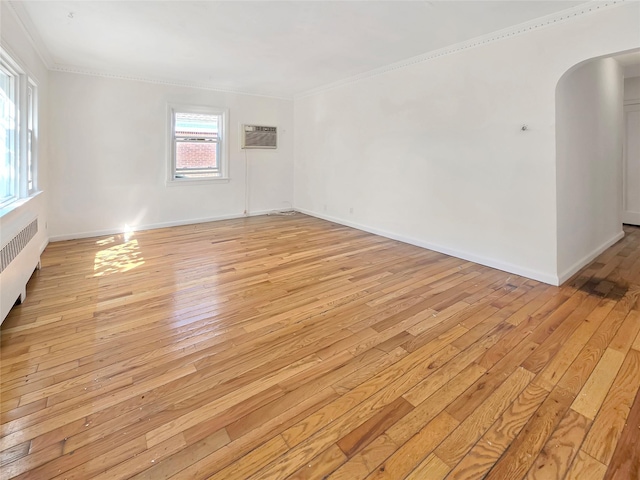 spare room featuring arched walkways, a wall unit AC, baseboards, light wood-type flooring, and crown molding