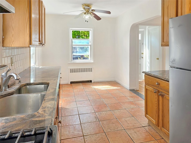 kitchen featuring tasteful backsplash, radiator, freestanding refrigerator, a sink, and light tile patterned flooring