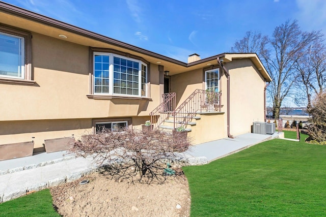 view of front facade with a front yard, central air condition unit, a chimney, and stucco siding