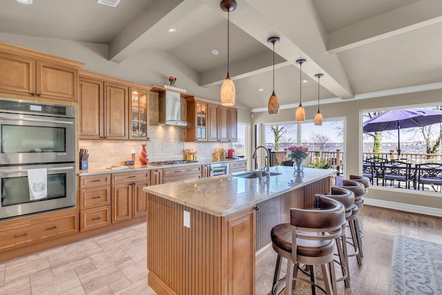 kitchen featuring vaulted ceiling with beams, stainless steel appliances, a sink, decorative backsplash, and wall chimney exhaust hood