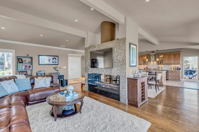 living room featuring vaulted ceiling with beams, a multi sided fireplace, wood finished floors, and a healthy amount of sunlight