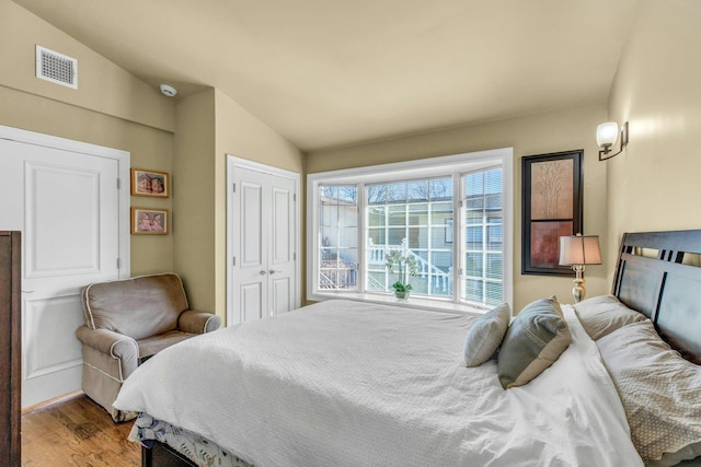 bedroom with lofted ceiling, a closet, visible vents, and wood finished floors