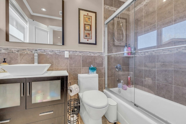 bathroom featuring toilet, enclosed tub / shower combo, ornamental molding, vanity, and tile walls