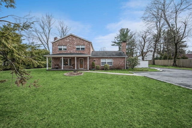 traditional-style home with fence, covered porch, a chimney, a front lawn, and brick siding