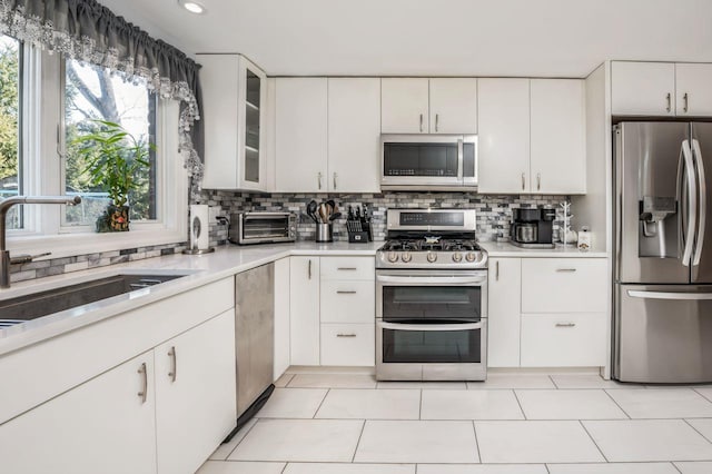 kitchen featuring a sink, white cabinetry, stainless steel appliances, light countertops, and decorative backsplash