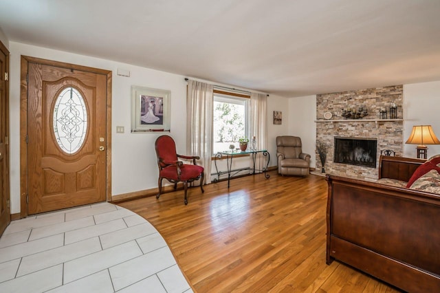 foyer featuring light wood finished floors, a stone fireplace, baseboards, and a baseboard radiator