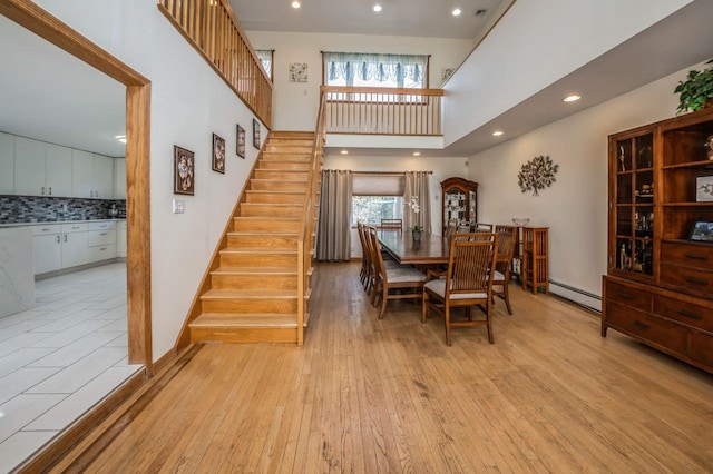 dining space featuring stairway, light wood-style flooring, recessed lighting, a towering ceiling, and baseboard heating