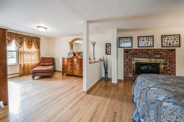 bedroom featuring a brick fireplace, wood finished floors, baseboards, and a baseboard radiator