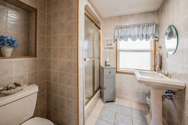 bathroom featuring tile patterned flooring, toilet, tile walls, and a shower with shower door