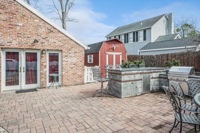 view of patio / terrace featuring fence, area for grilling, an outdoor structure, a storage unit, and french doors