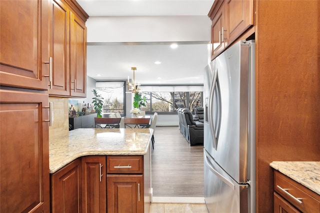 kitchen with brown cabinetry, open floor plan, stainless steel refrigerator with ice dispenser, and light stone countertops