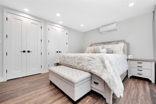 bedroom with recessed lighting, wood finished floors, a wall mounted air conditioner, and two closets