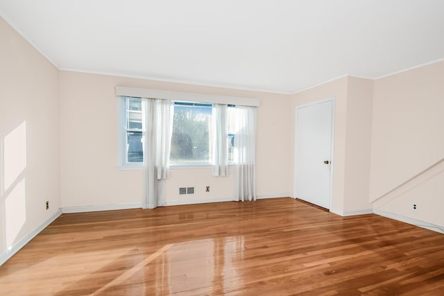 unfurnished room with ornamental molding, light wood-type flooring, visible vents, and baseboards