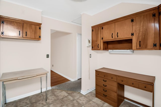 kitchen featuring brown cabinetry, vaulted ceiling, crown molding, and baseboards