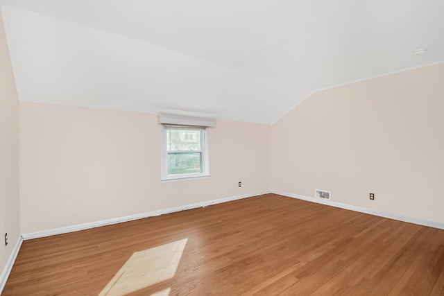 additional living space with light wood-style floors, baseboards, visible vents, and vaulted ceiling