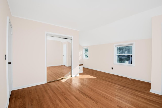 unfurnished bedroom with a closet, ornamental molding, vaulted ceiling, light wood-type flooring, and baseboards