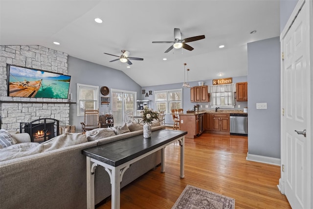 living room featuring light wood finished floors, lofted ceiling, recessed lighting, a ceiling fan, and a stone fireplace