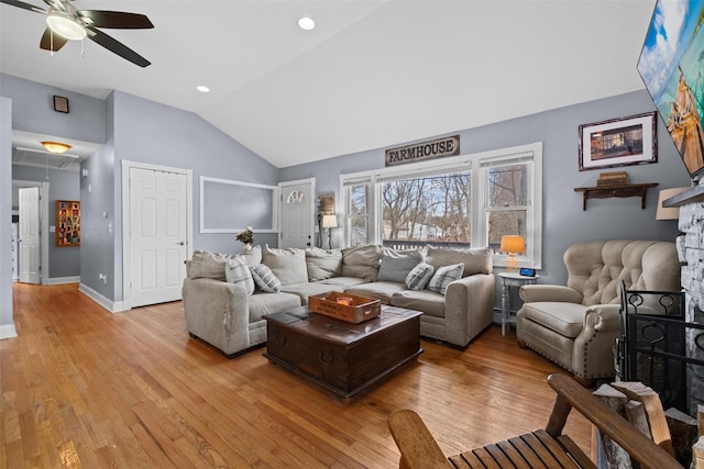 living room with lofted ceiling, a fireplace, a ceiling fan, light wood finished floors, and attic access