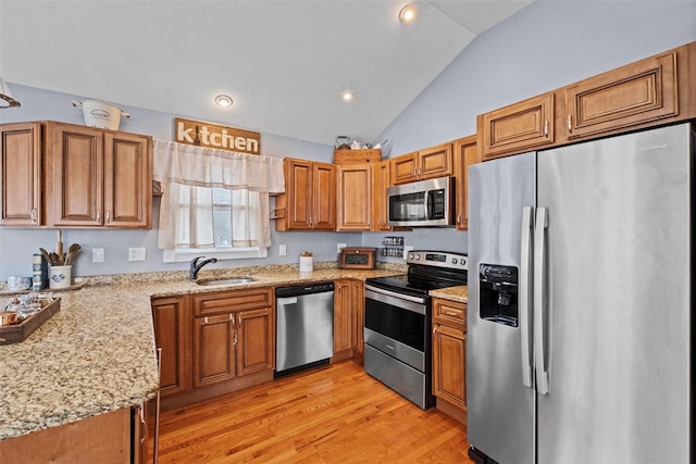 kitchen with light stone counters, stainless steel appliances, brown cabinetry, a sink, and light wood-type flooring