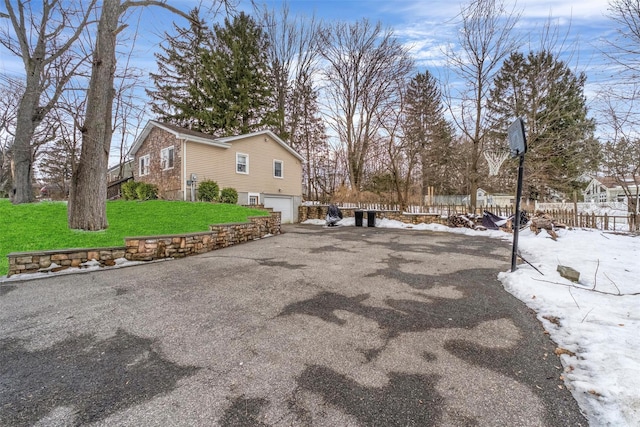 view of snowy exterior with driveway, a garage, fence, and a lawn