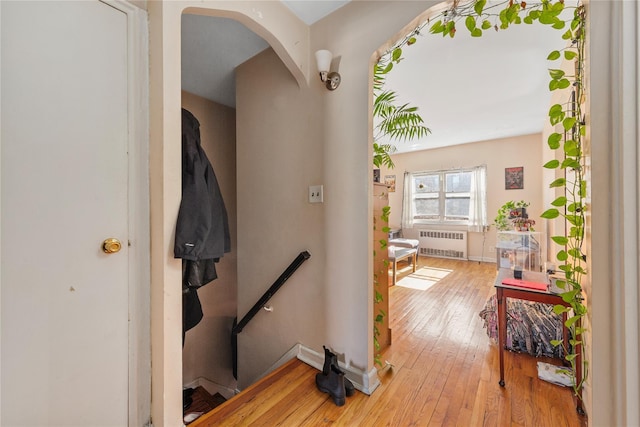 corridor with baseboards, arched walkways, radiator, hardwood / wood-style flooring, and an upstairs landing