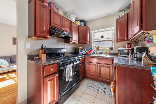 kitchen with light tile patterned floors, under cabinet range hood, a sink, black gas stove, and backsplash