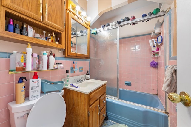 bathroom featuring tile walls, tasteful backsplash, toilet, combined bath / shower with glass door, and vanity