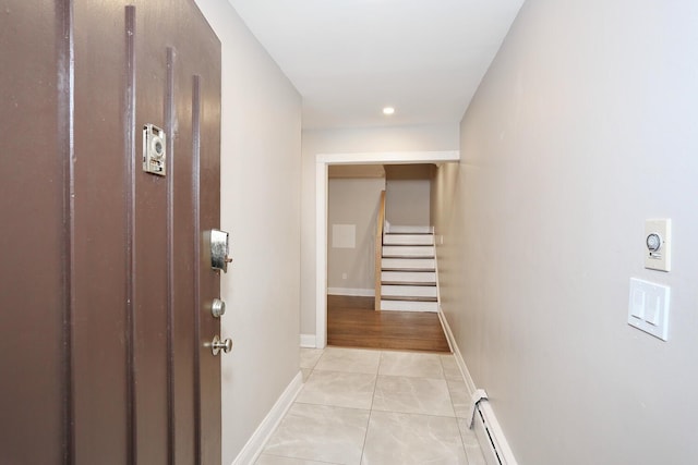 hallway with light tile patterned floors, baseboards, stairway, and a baseboard heating unit