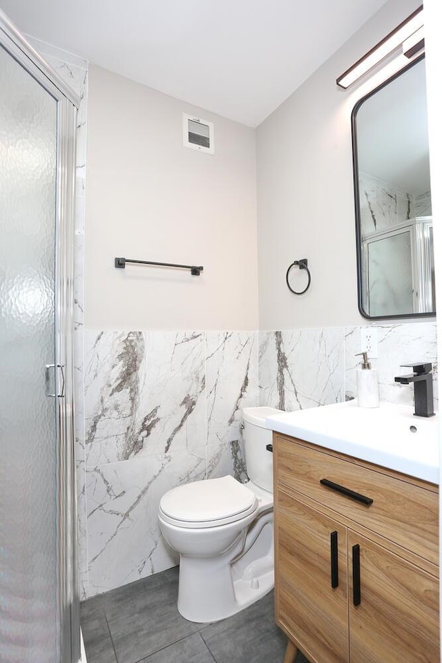 bathroom featuring tile walls, visible vents, toilet, a shower stall, and vanity