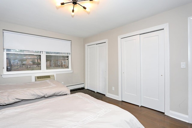 bedroom featuring baseboards, a wall unit AC, a baseboard radiator, wood finished floors, and two closets