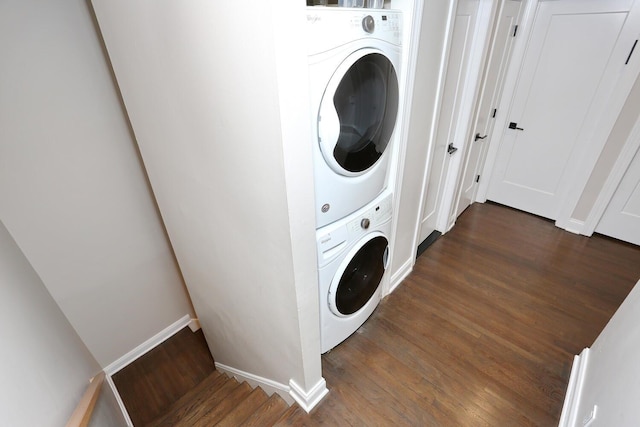 clothes washing area featuring laundry area, stacked washer and clothes dryer, baseboards, and wood finished floors