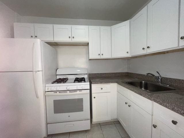 kitchen with white appliances, dark countertops, a sink, and white cabinets