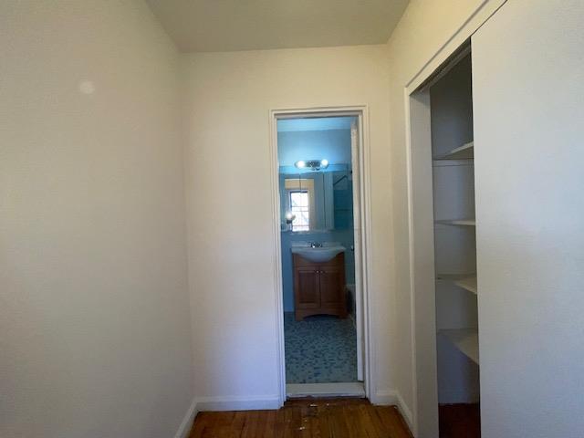 hall featuring dark wood-style floors, a sink, and baseboards