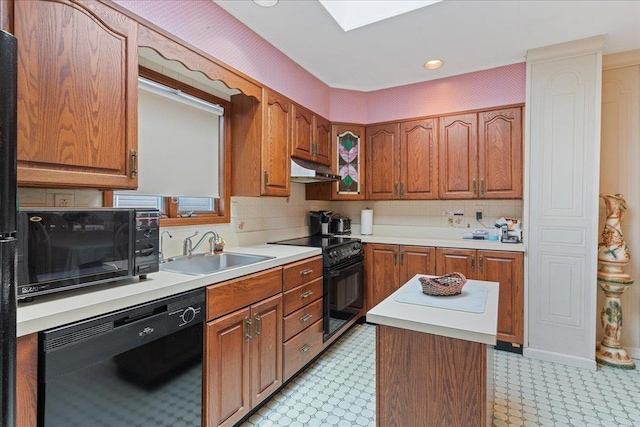 kitchen featuring under cabinet range hood, a sink, light countertops, black appliances, and brown cabinetry