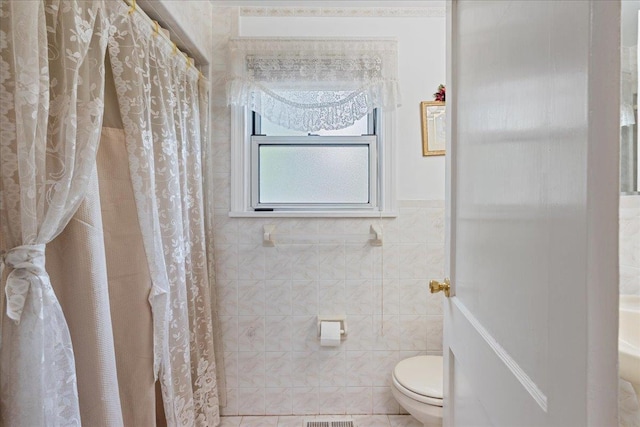 bathroom with toilet, a shower with curtain, visible vents, and tile walls