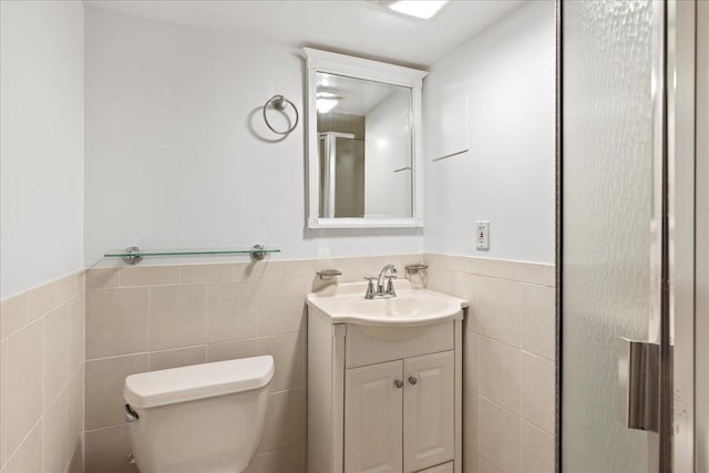 full bathroom featuring toilet, vanity, tile walls, wainscoting, and a stall shower