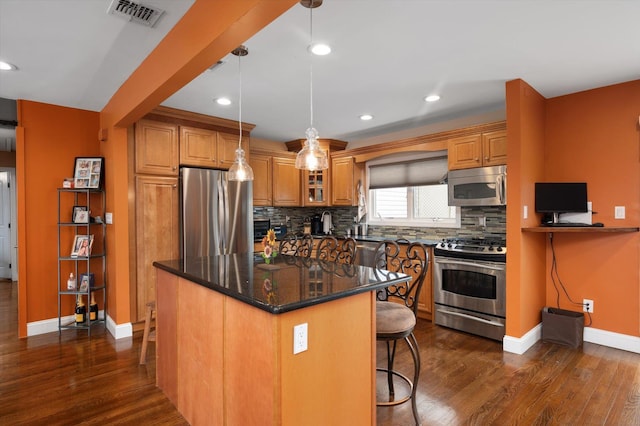 kitchen with stainless steel appliances, visible vents, a kitchen breakfast bar, tasteful backsplash, and brown cabinetry