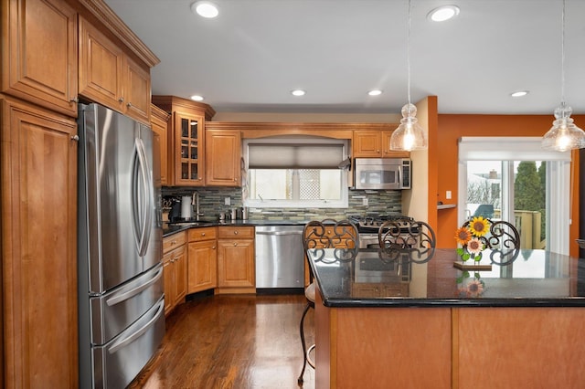 kitchen with appliances with stainless steel finishes, dark wood-style flooring, backsplash, and brown cabinets