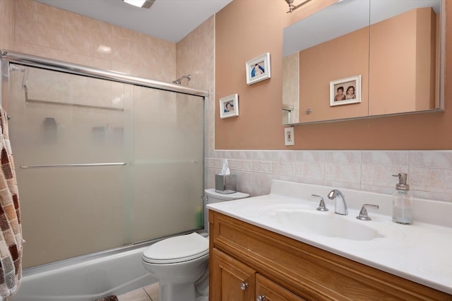 full bath with toilet, a wainscoted wall, combined bath / shower with glass door, vanity, and tile walls