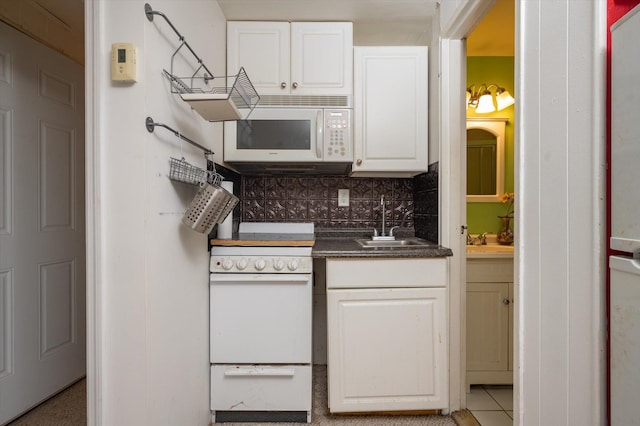 kitchen featuring white appliances, a sink, white cabinets, tasteful backsplash, and dark countertops